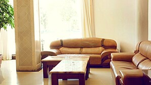 A spacious living room with a leather sofa, a wooden coffee table, and a large window with curtains. - GreenTree Inn Lianyungang Ganyu South Station Express Hotel (Lianyungang)