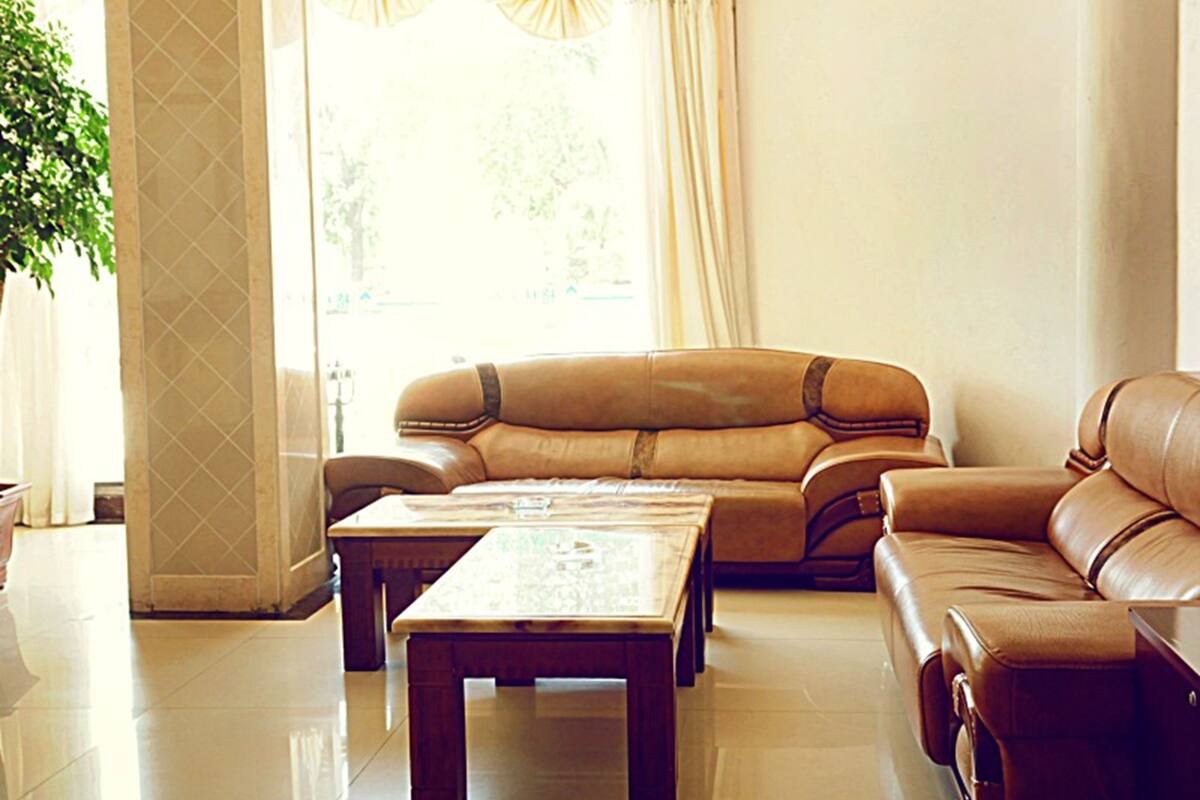 A spacious living room with a leather sofa, a wooden coffee table, and a large window with curtains.