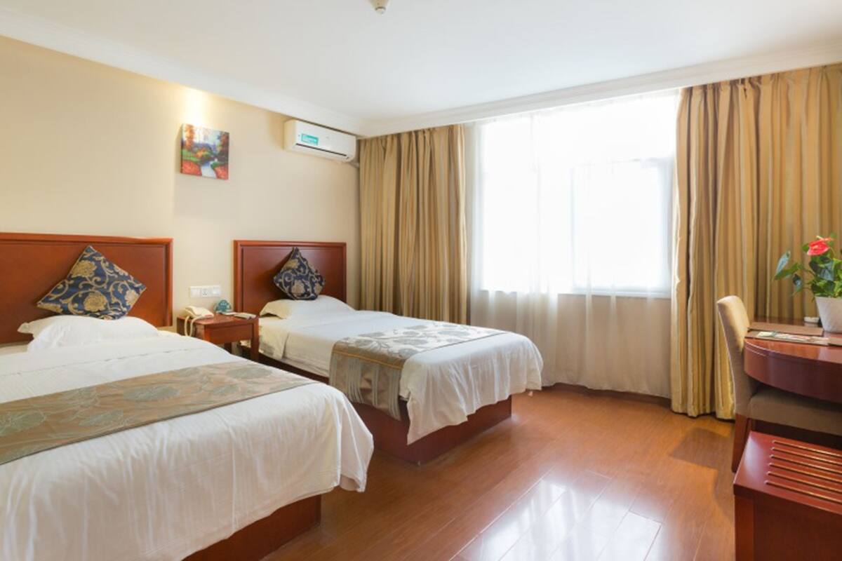 Une chambre d’hôtel avec deux lits, un bureau, une chaise et une grande fenêtre avec des rideaux.
