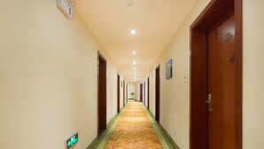 A hotel hallway with a carpeted floor, wooden doors, and a sign indicating the direction to the elevators.