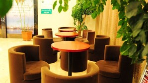 A seating area with round tables and chairs, potted plants, and a view of a body of water.
