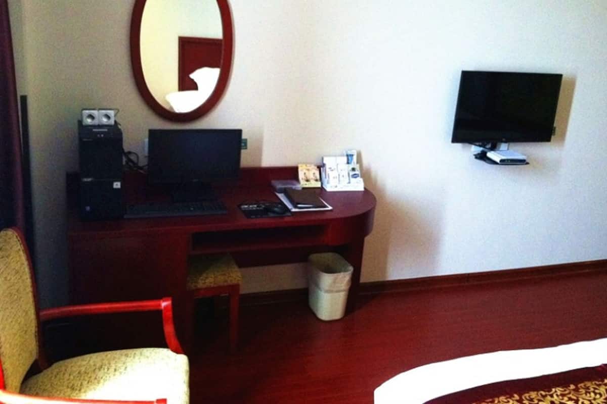 A hotel room with a wooden desk, a computer, a television, and a chair.