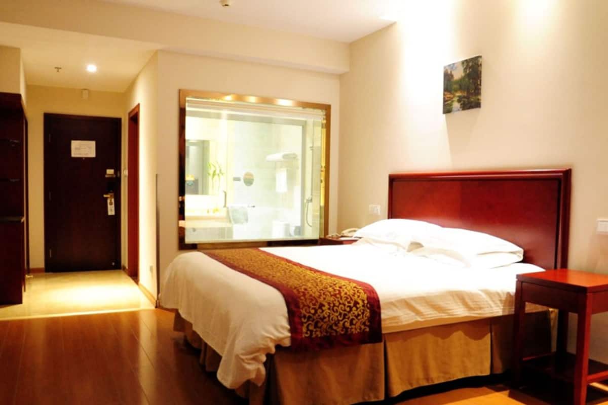 A hotel room with a large bed, a wooden headboard, a bedside table, and a large mirror.