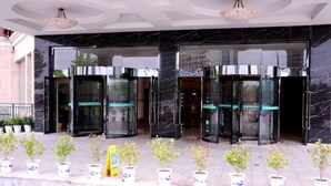 A hotel entrance with black marble doors, potted plants, and a yellow sign.