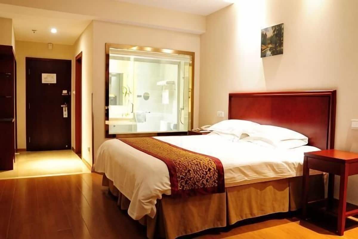 A hotel room with a bed, a bedside table, a mirror, and a door leading to a bathroom.
