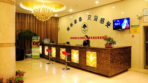 A hotel reception area with a receptionist, a large chandelier, a TV screen, and a wall with signage.