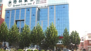 Un moderno edificio de hotel con una amplia fachada de vidrio, un letrero llamativo de GreenTree Inn y un área de estacionamiento al frente.