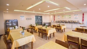 A dining area with tables and chairs, a refrigerator, and a buffet counter. - GreenTree Inn GuangDe County ZhongYang LeCheng Hotel (Xuancheng)