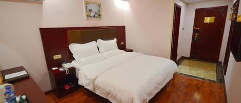 A hotel room with a large bed, a bedside table with a phone, a water bottle, and a small table with a tray.