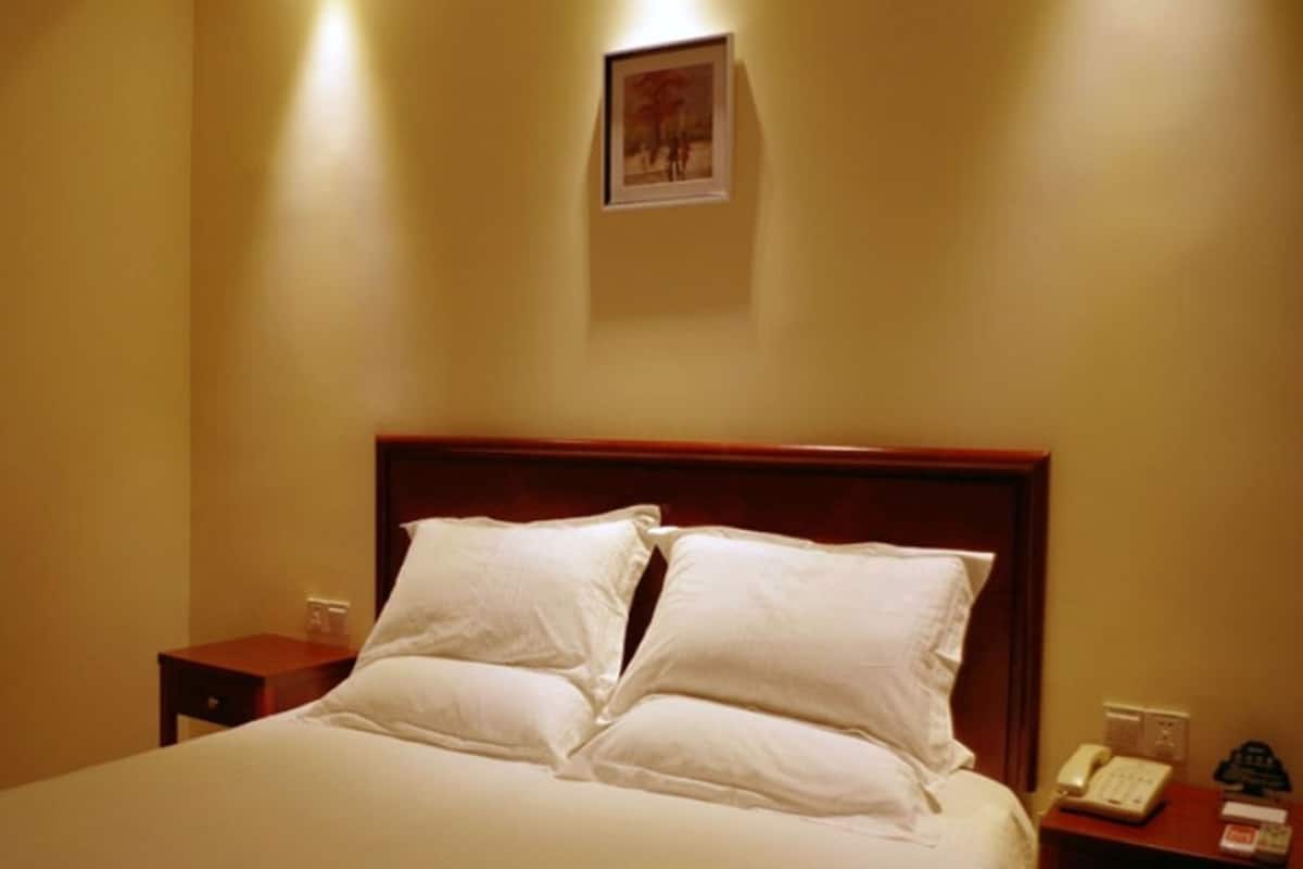 Ein ordentlich bezogenes Bett mit weißen Leinentextilien und Kissen, ein hölzernes Kopfteil, ein Nachttisch mit Lampe sowie ein an der Wand befestigtes Telefon.