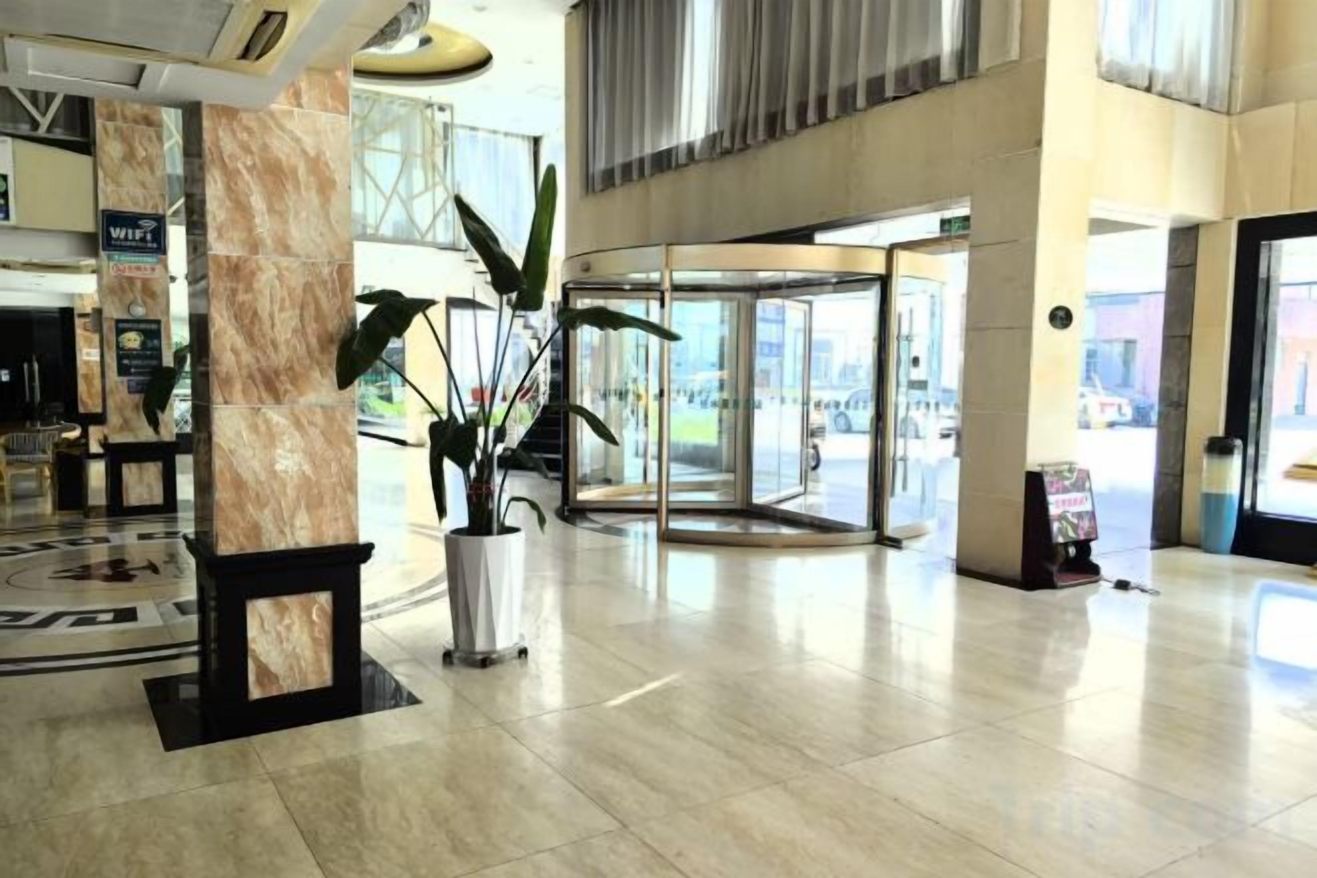 A hotel lobby with a marble floor, a reception desk, a potted plant, and a revolving door.