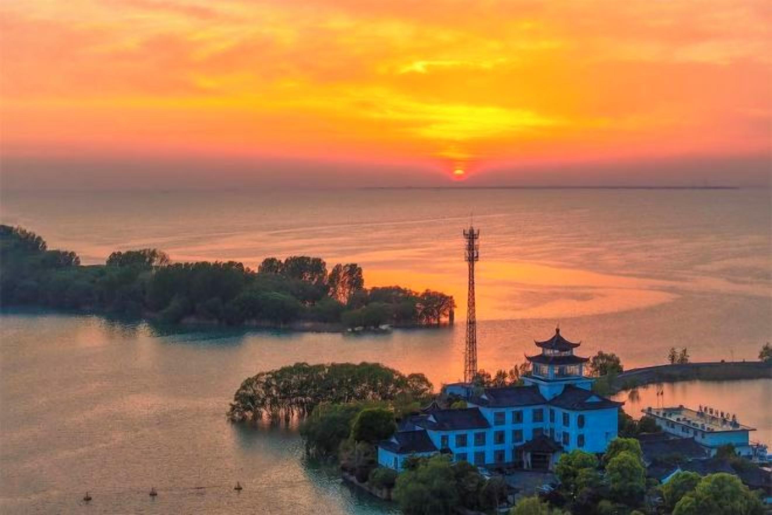 A coastal scene with a traditional building, a tower, and a sunset over the water.