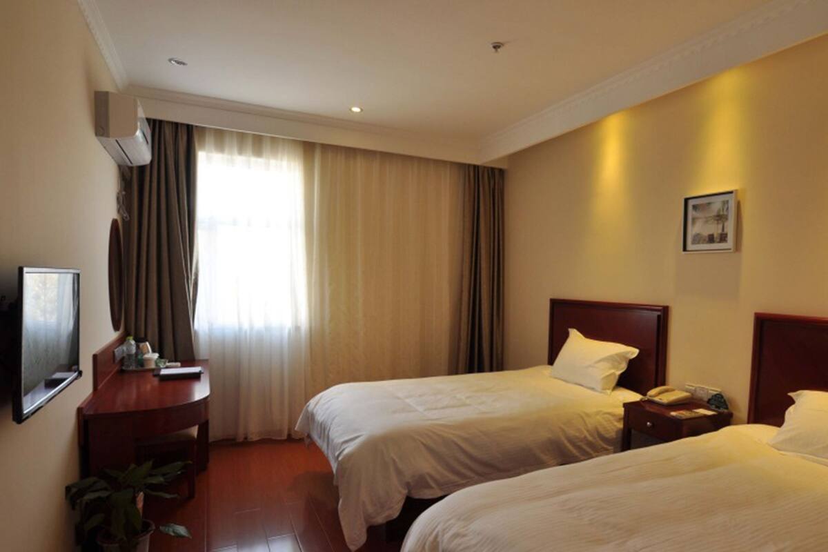 Ein Hotelzimmer mit zwei Betten, einem Schreibtisch, einem Fernseher und einer Zimmerpflanze.