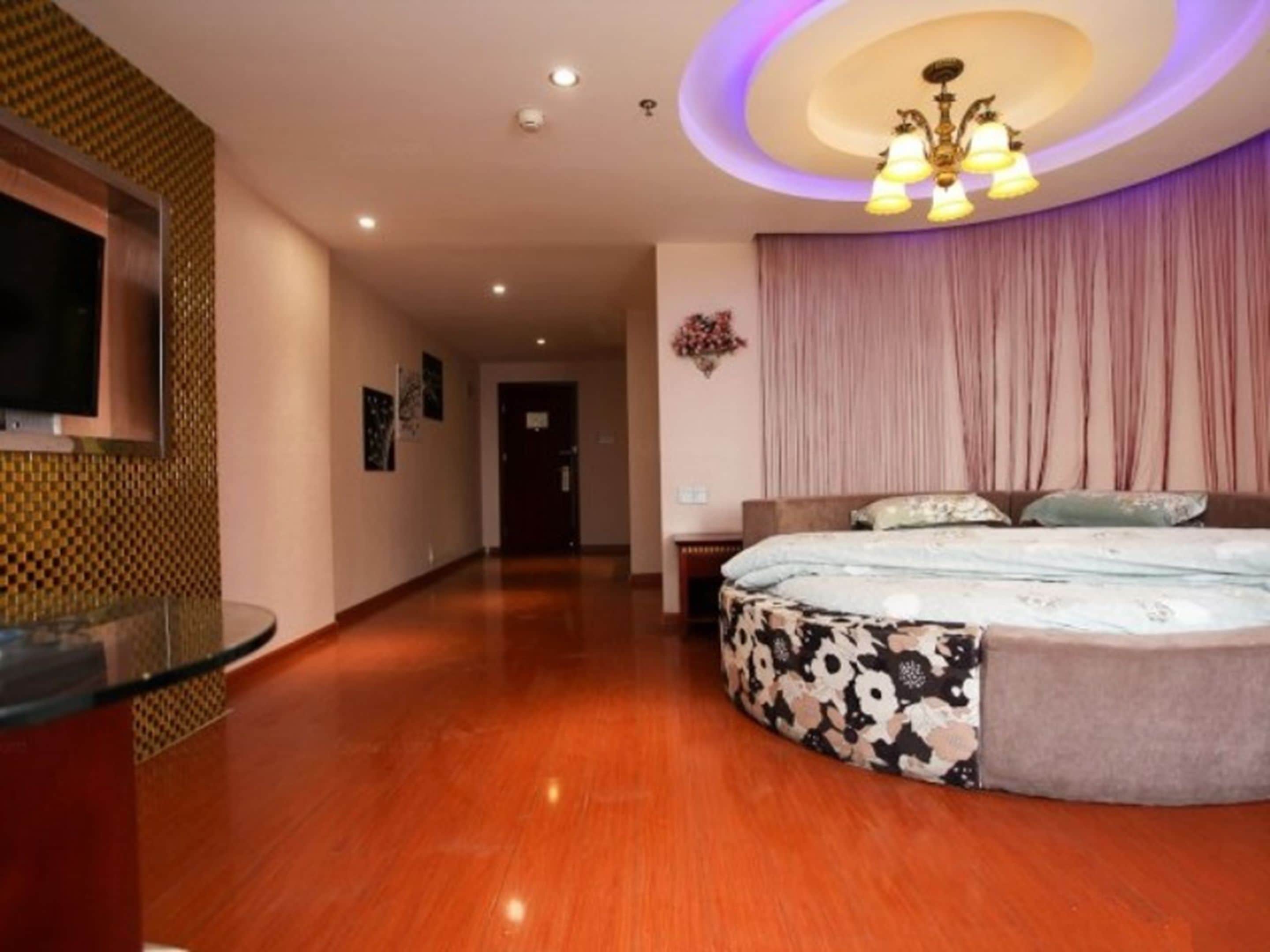 A hotel room with a large bed, a glass coffee table, a TV mounted on the wall, and a chandelier.