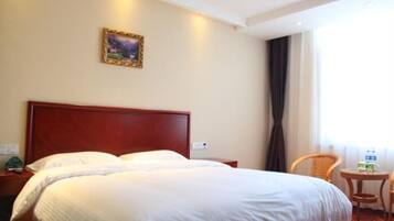 A hotel room with a large bed, a nightstand, a small table with a chair, and a window with curtains.