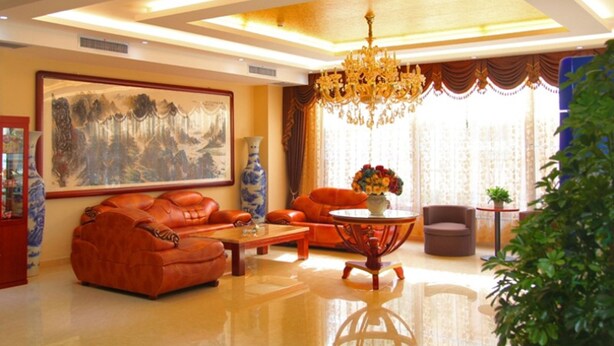 A spacious living room with leather sofas, a coffee table, a chandelier, and a large painting on the wall.