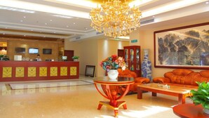 A hotel lobby with a reception desk, a chandelier, a sofa, and a coffee table.