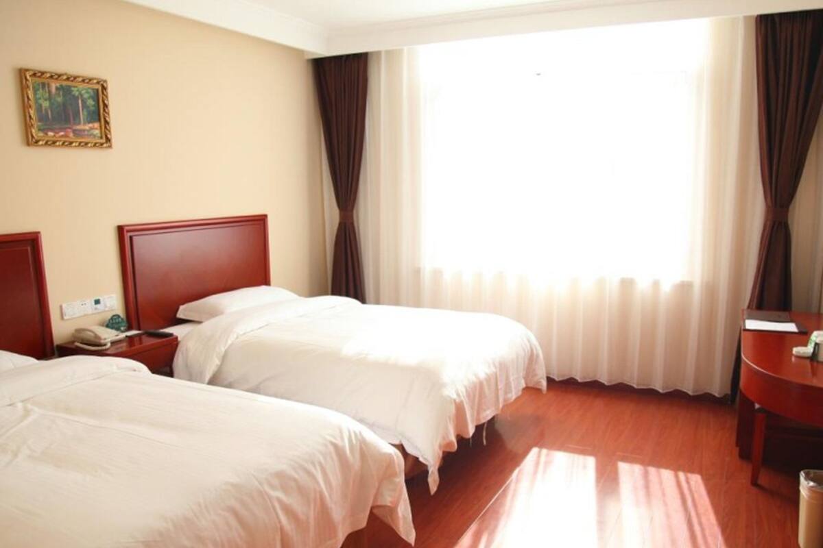 Habitación de hotel con dos camas, cabecero de madera, mesita de noche con teléfono y ventana con cortinas.