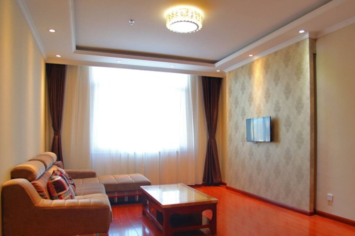 Un salón espacioso con un ventanal grande, un conjunto de sofás, una mesa de centro y un televisor de pantalla plana montado en la pared.