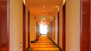 A hotel hallway with a carpeted floor, doors on both sides, and a light at the end.