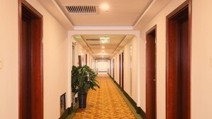 Un couloir d'hôtel avec un sol recouvert de moquette, des portes en bois et une plante en pot.