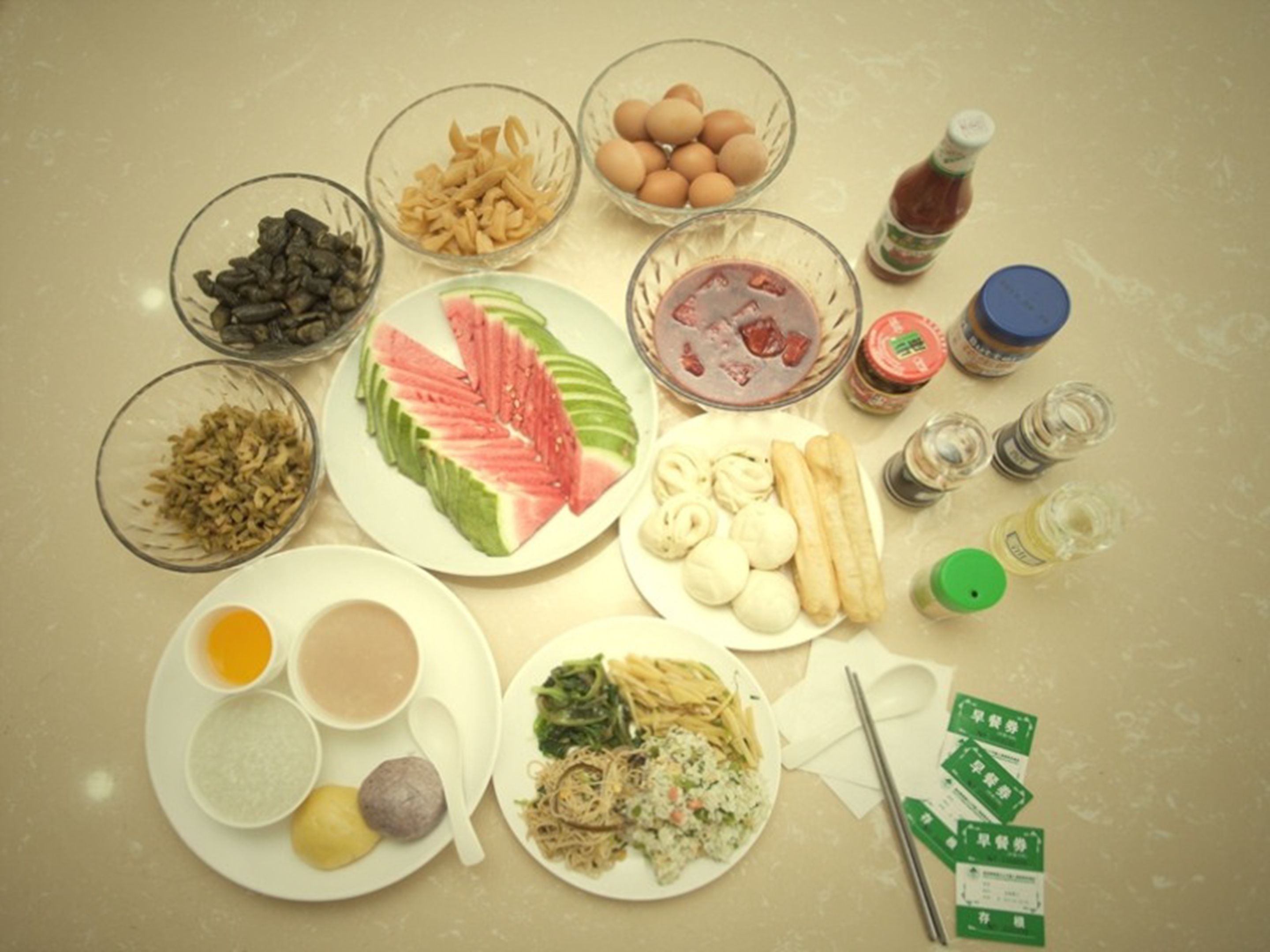 A table with various food items and condiments, including bowls of nuts, sliced watermelon, eggs, and a plate of noodles.