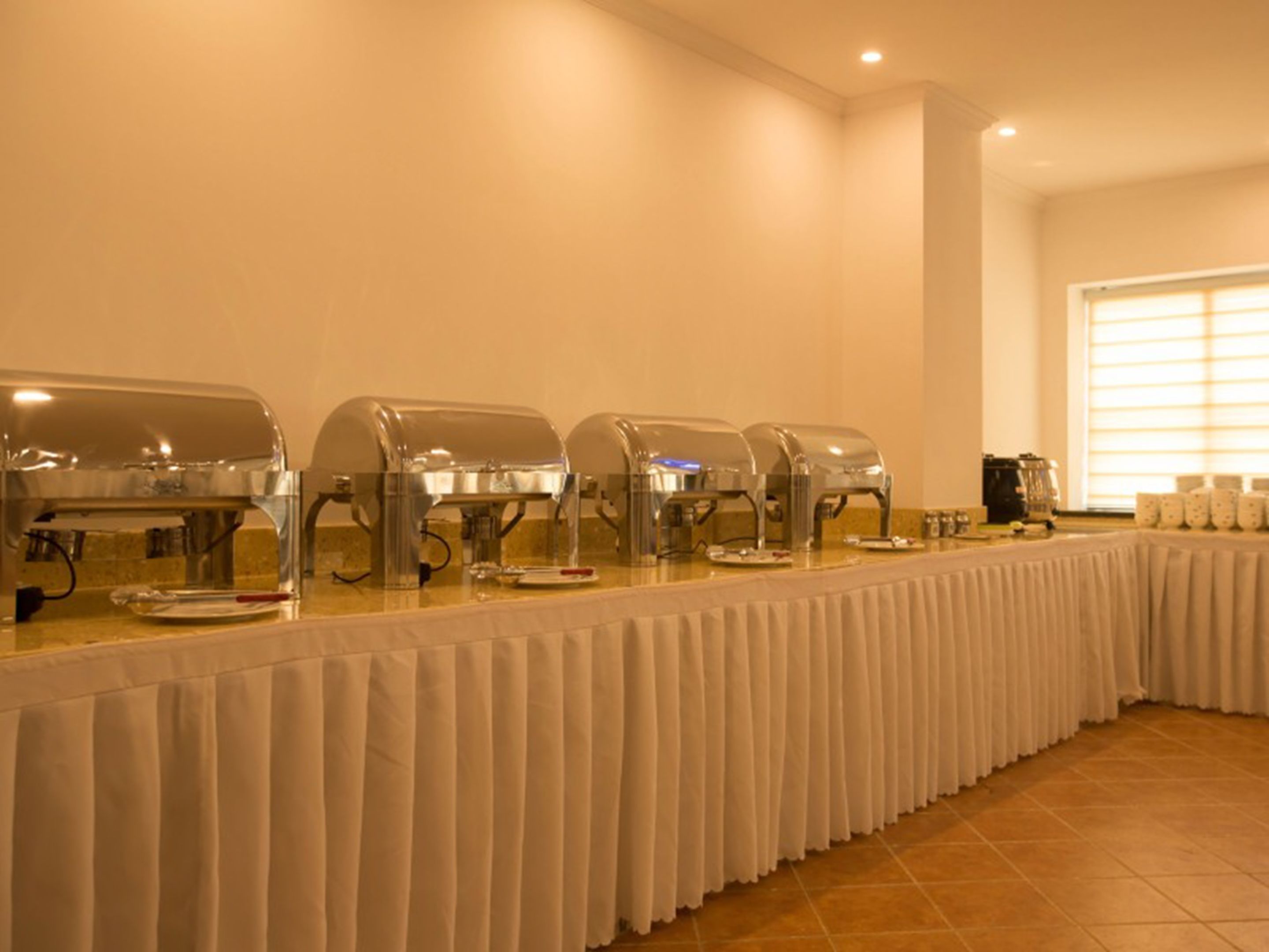 A buffet setup with multiple self-service coffee machines and a long table covered with a white tablecloth.
