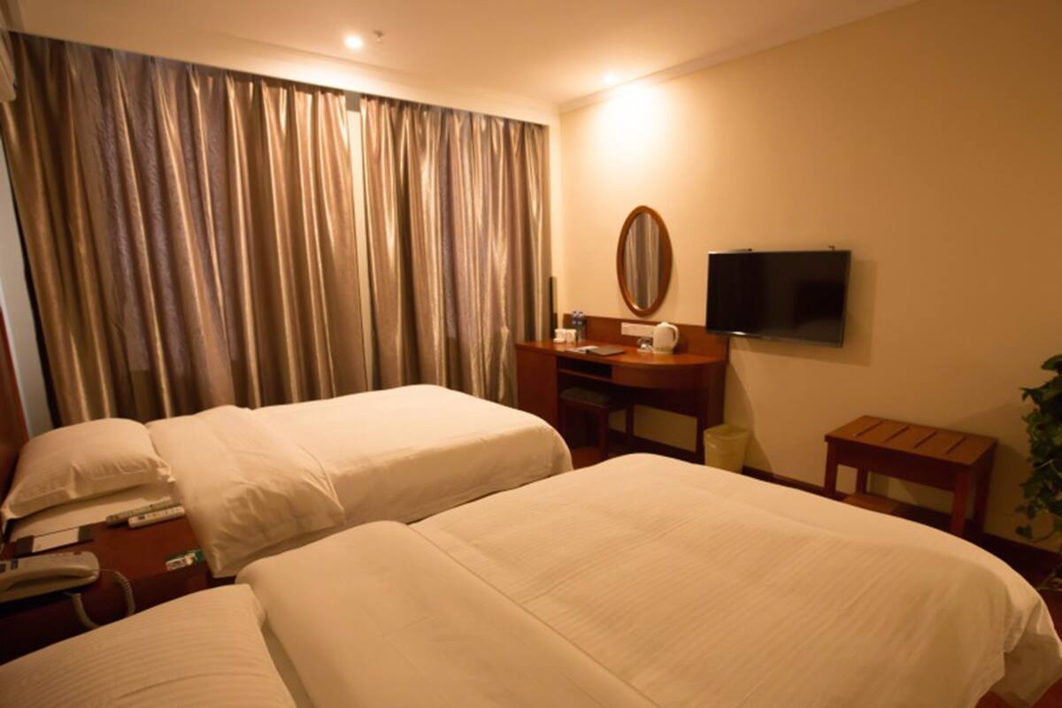 A hotel room with two beds, a desk, a chair, a TV, and a window with curtains.
