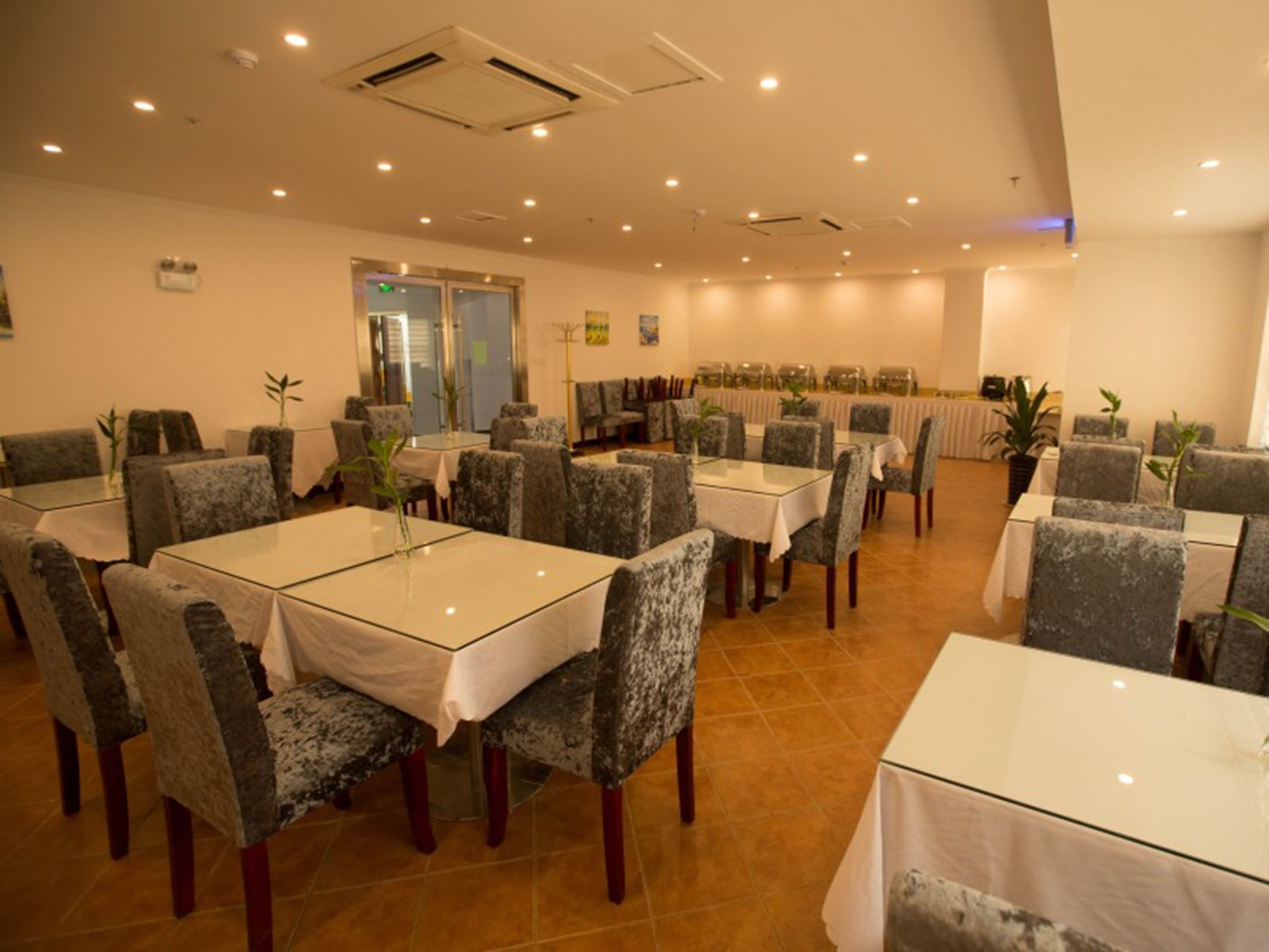 A dining area with tables and chairs, a kitchen in the background, and a door leading outside.
