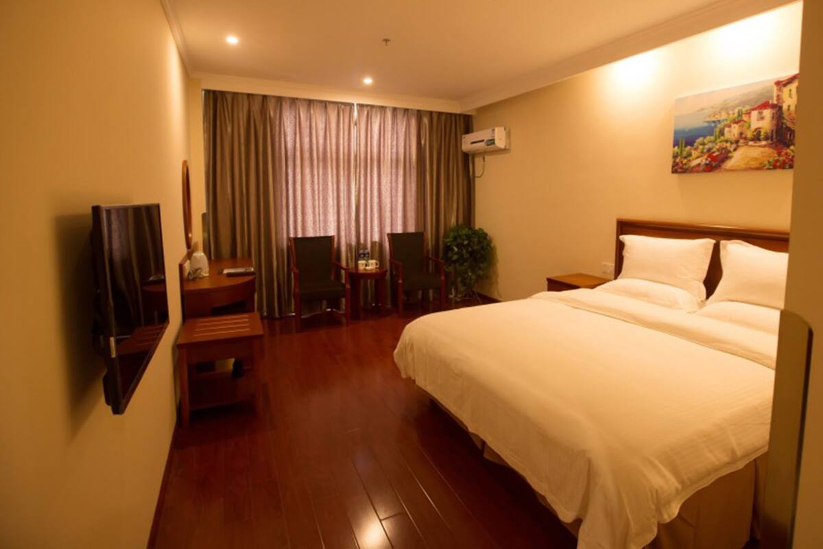 A hotel room with a large bed, a desk with a chair, a television, and a painting on the wall.