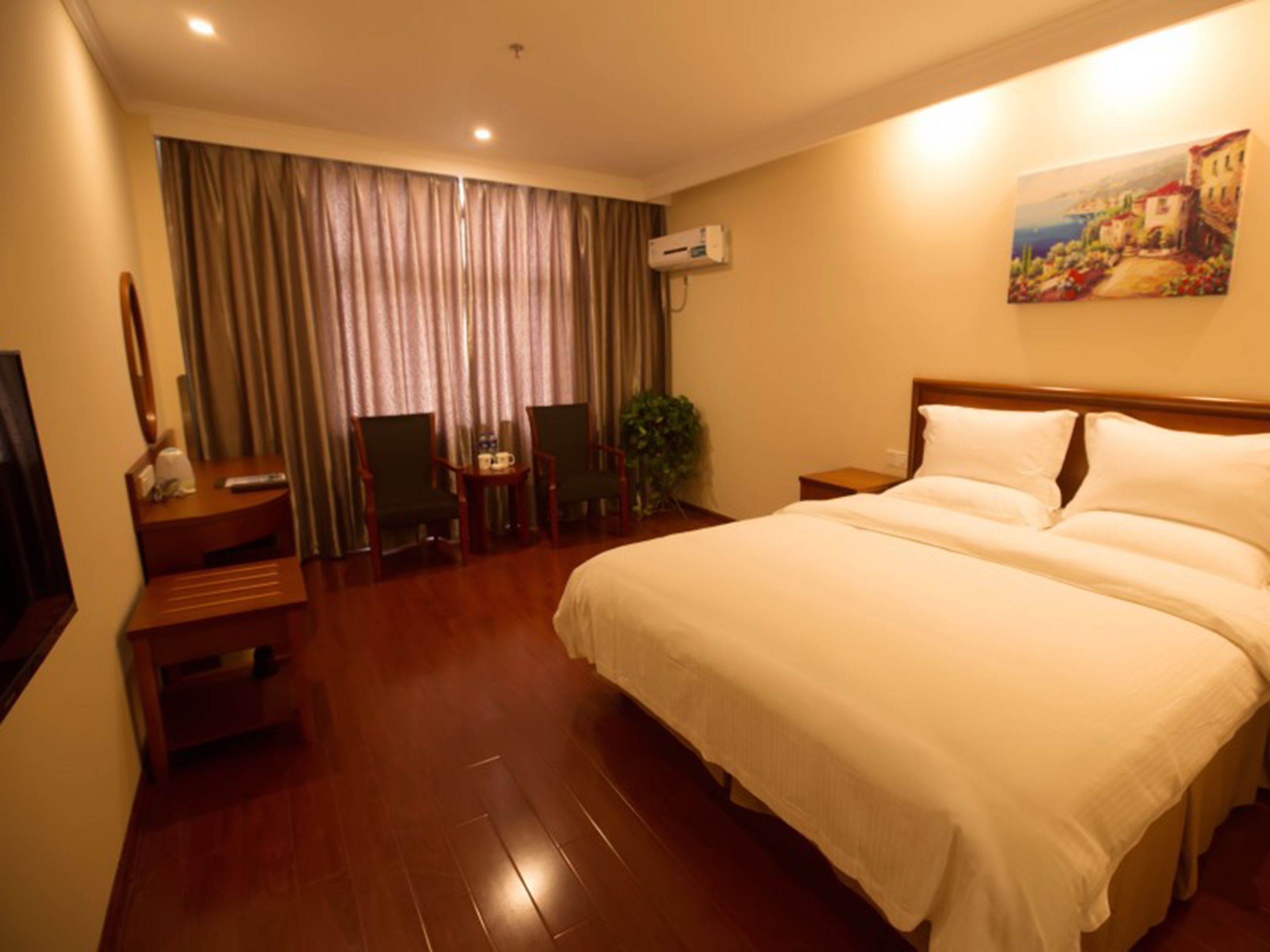 A hotel room with a large bed, a desk with a chair, a television, and a painting on the wall.