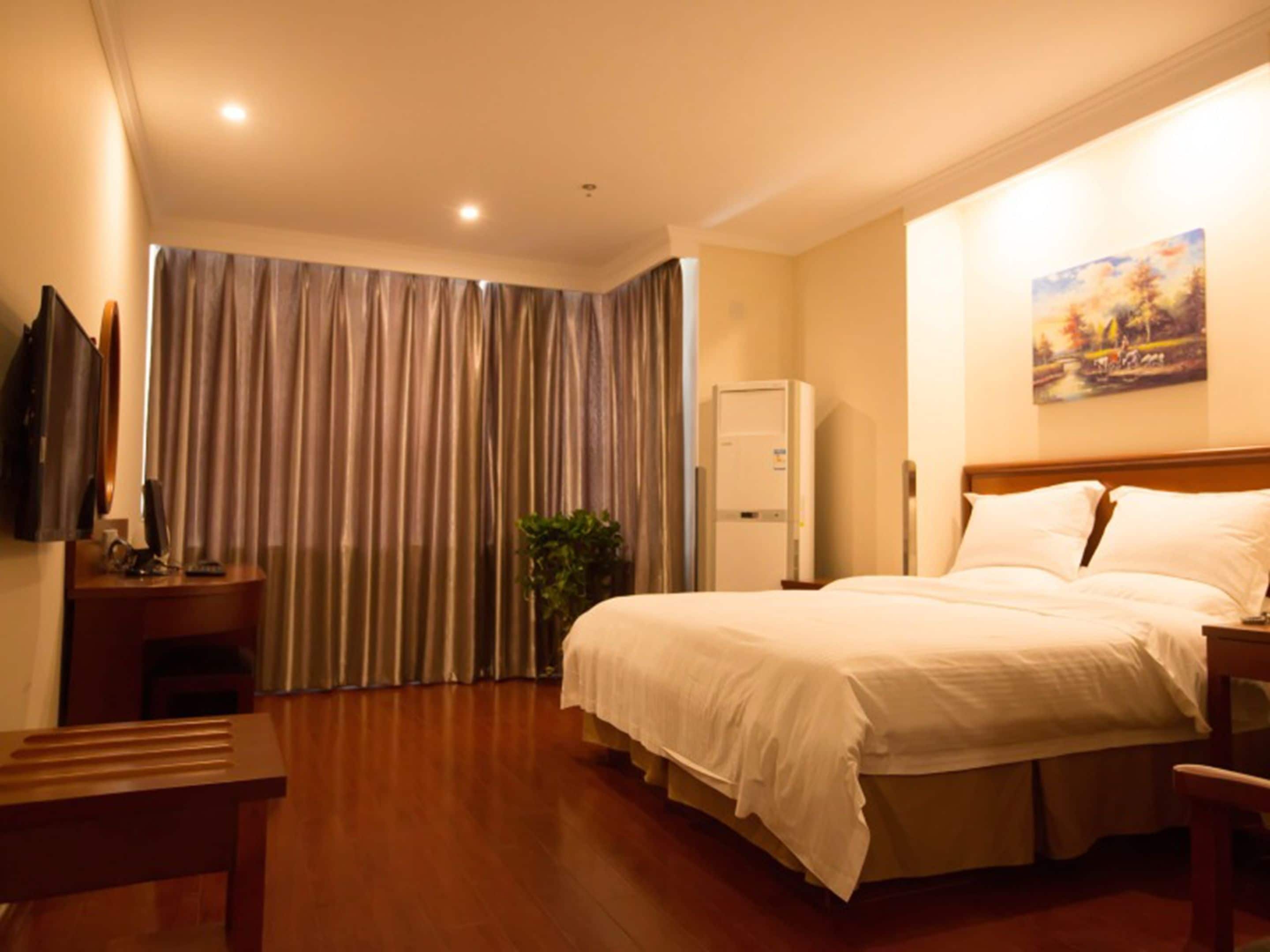 A hotel room with a bed, a desk, a television, a refrigerator, and a window with curtains.