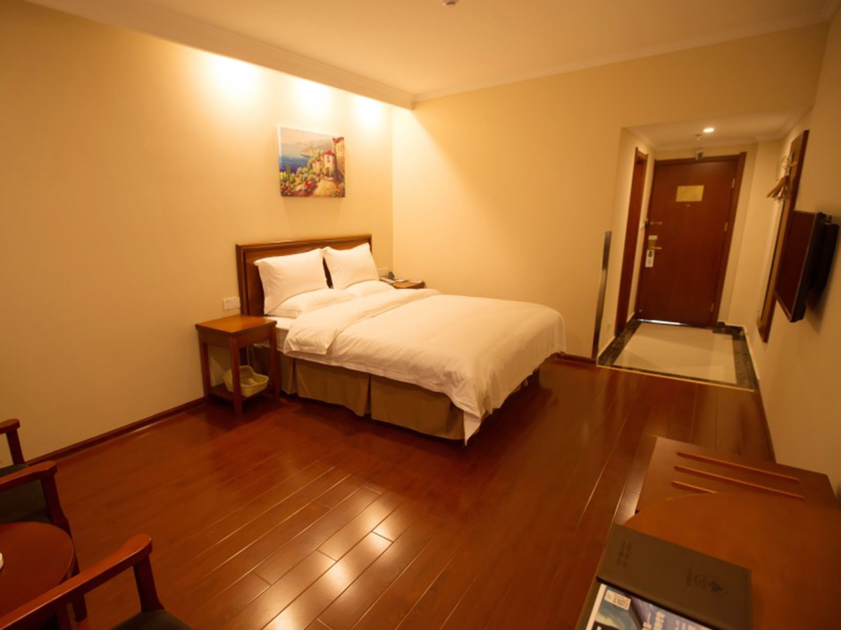 Una camera d'hotel con un letto, un comodino, un pavimento in legno, un quadro appeso al muro e una porta.