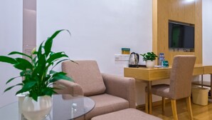 A modern room with a glass table, two beige armchairs, a wooden desk, a television, and a potted plant. - GreenTree Inn Anshun Xihang Road Hotel (Anshun)