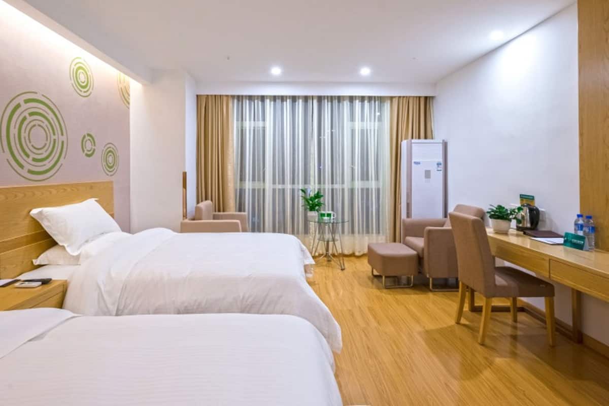 Hotellihuone, jossa on kaksi sänkyä, työpöytä, tuoleja, jääkaappi ja ikkuna, jossa on verhot.