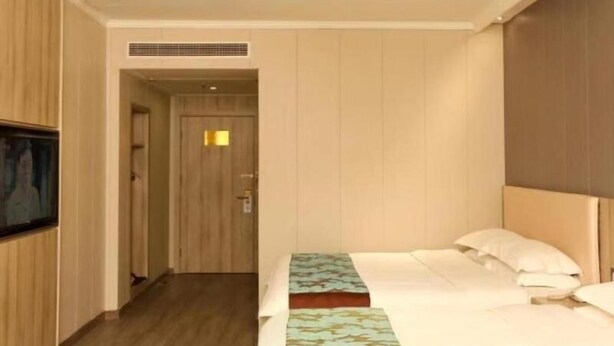 A hotel room with a bed, a television on the wall, and a door leading to another room. - GreenTree Inn JiangSu YanCheng JianHu ShangGang Bus Station Freeway 204 Express Hotel (Yancheng)
