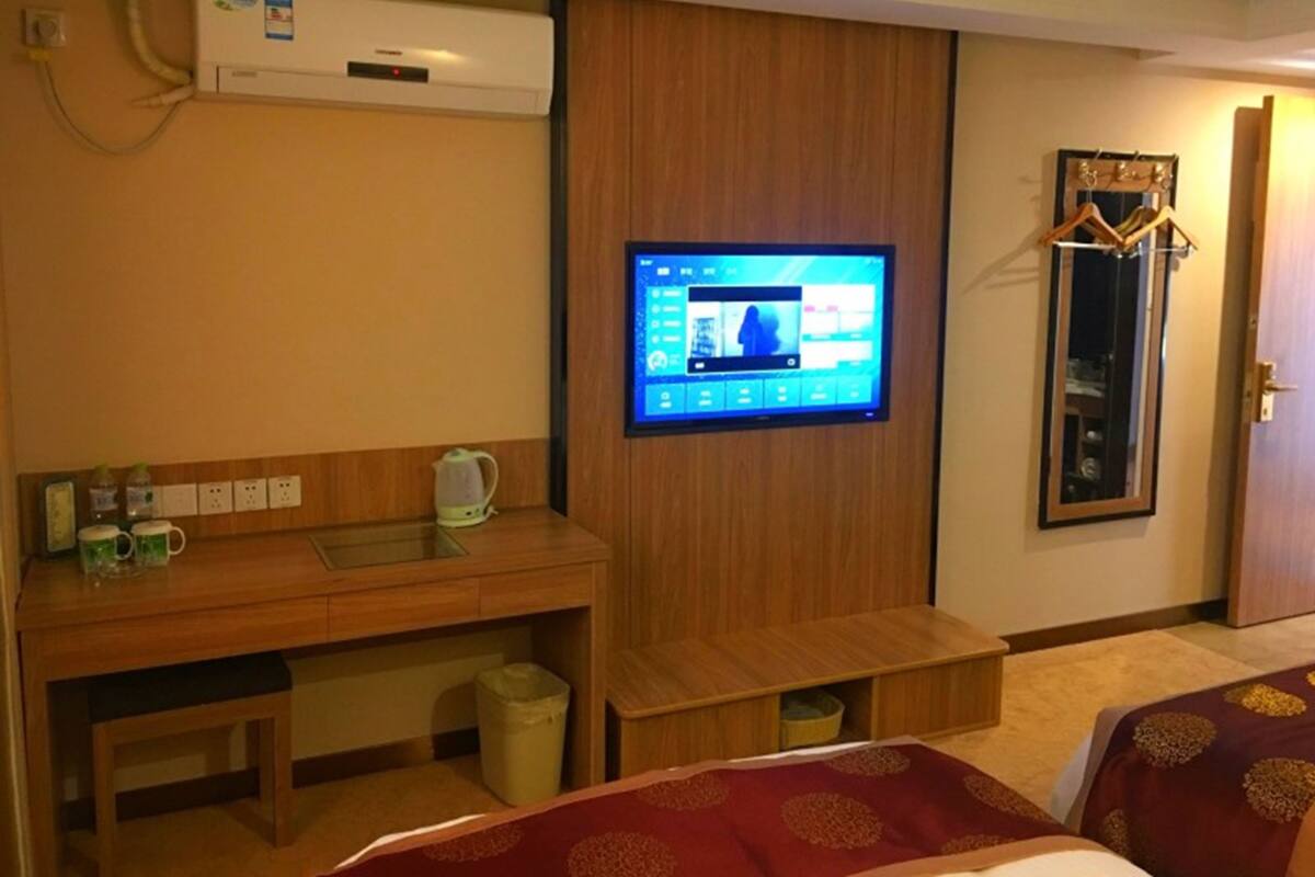 Een hotelkamer met een houten bureau, een aan de muur bevestigde televisie, een spiegel en twee bedden met decoratieve beddengoed.