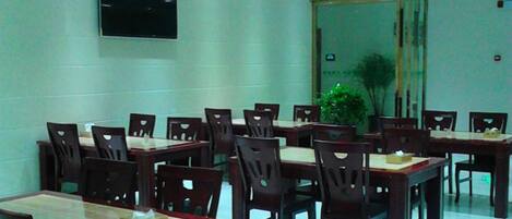 A dining area with multiple tables and chairs, a television mounted on the wall, and a trash bin.