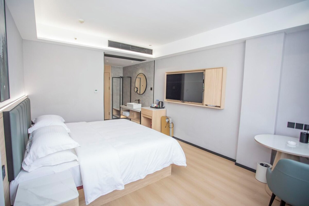 A hotel room with a bed, a desk, a mirror, and a television.