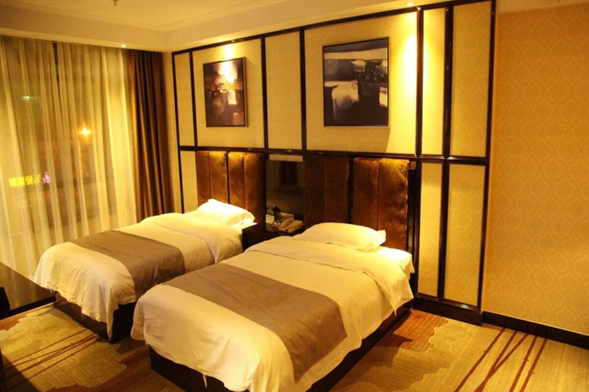 A hotel room with two beds, a large window with curtains, and a wall-mounted artwork.