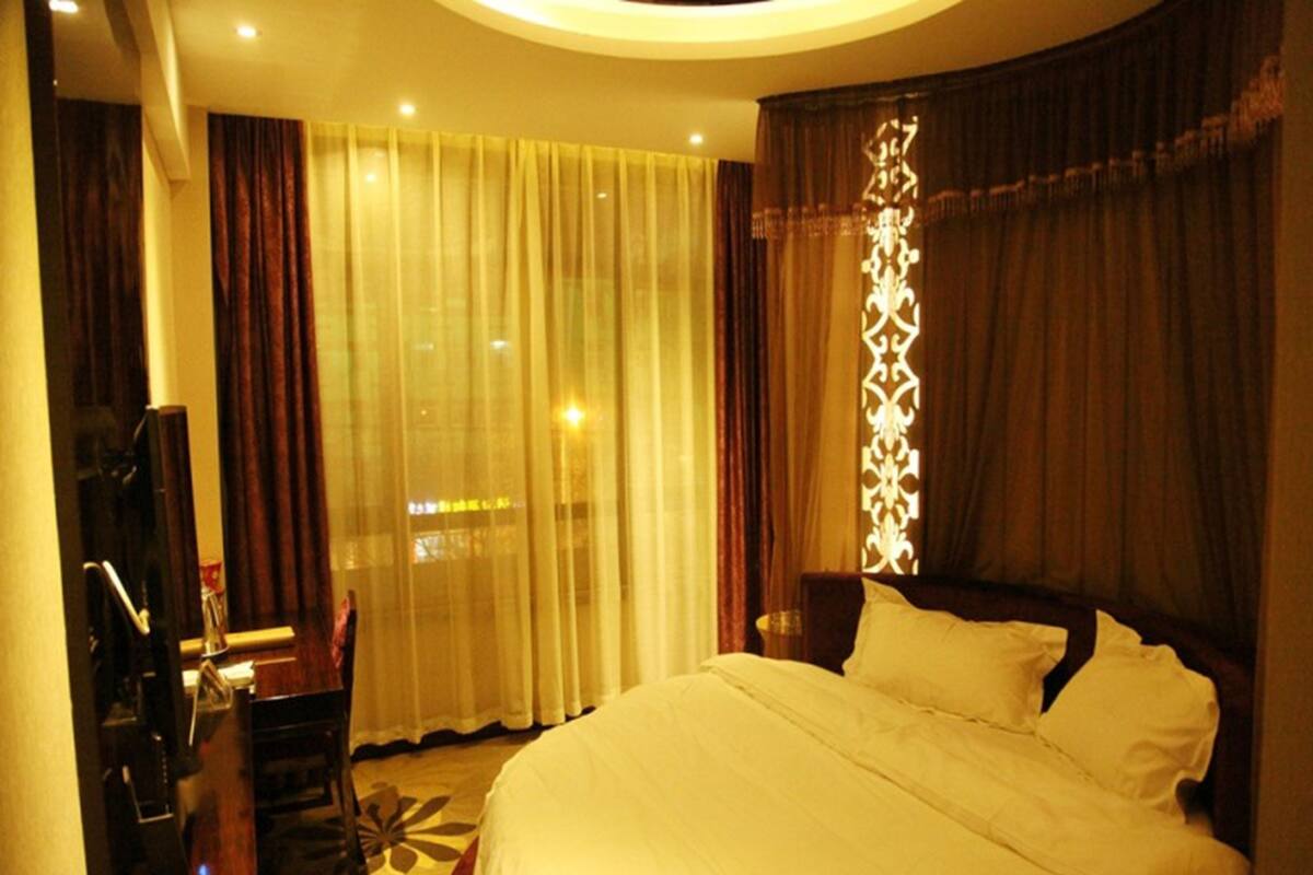 A hotel room with a large bed, a desk, a television, and a window with curtains.