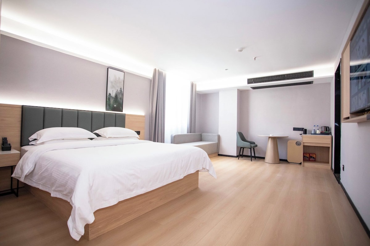 A modern hotel room with a large bed, bedside table, a desk with a chair, and a TV mounted on the wall.