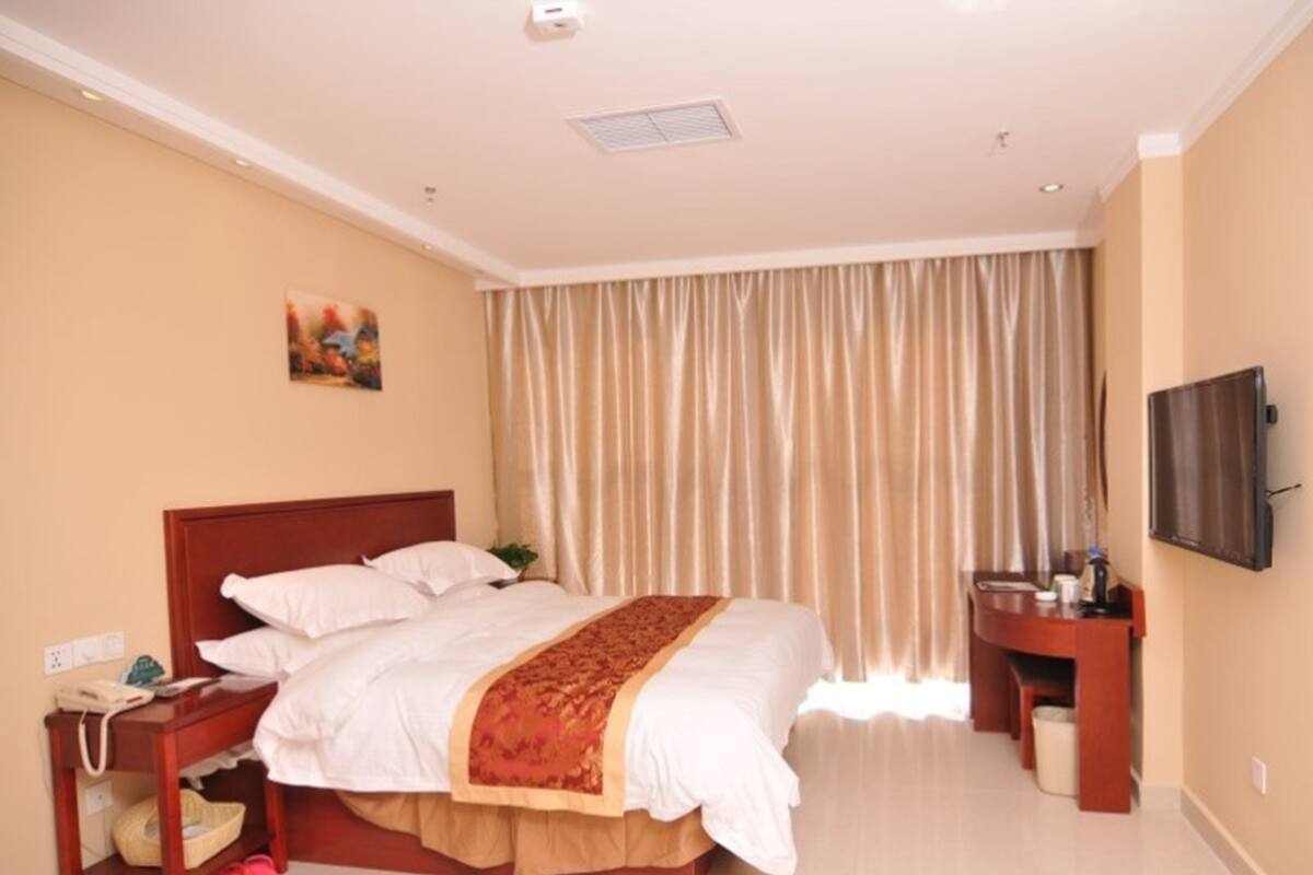 Ein Hotelzimmer mit einem großen Bett, einem Nachttisch mit Telefon, einem an der Wand montierten Fernseher und einem Fenstervorhang.