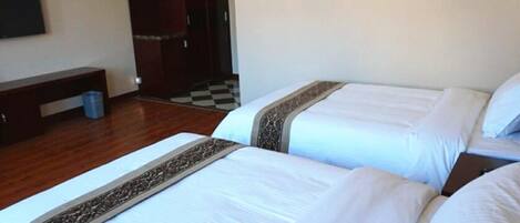 Quarto de hotel com duas camas, um banco, um guarda-roupa e uma televisão.