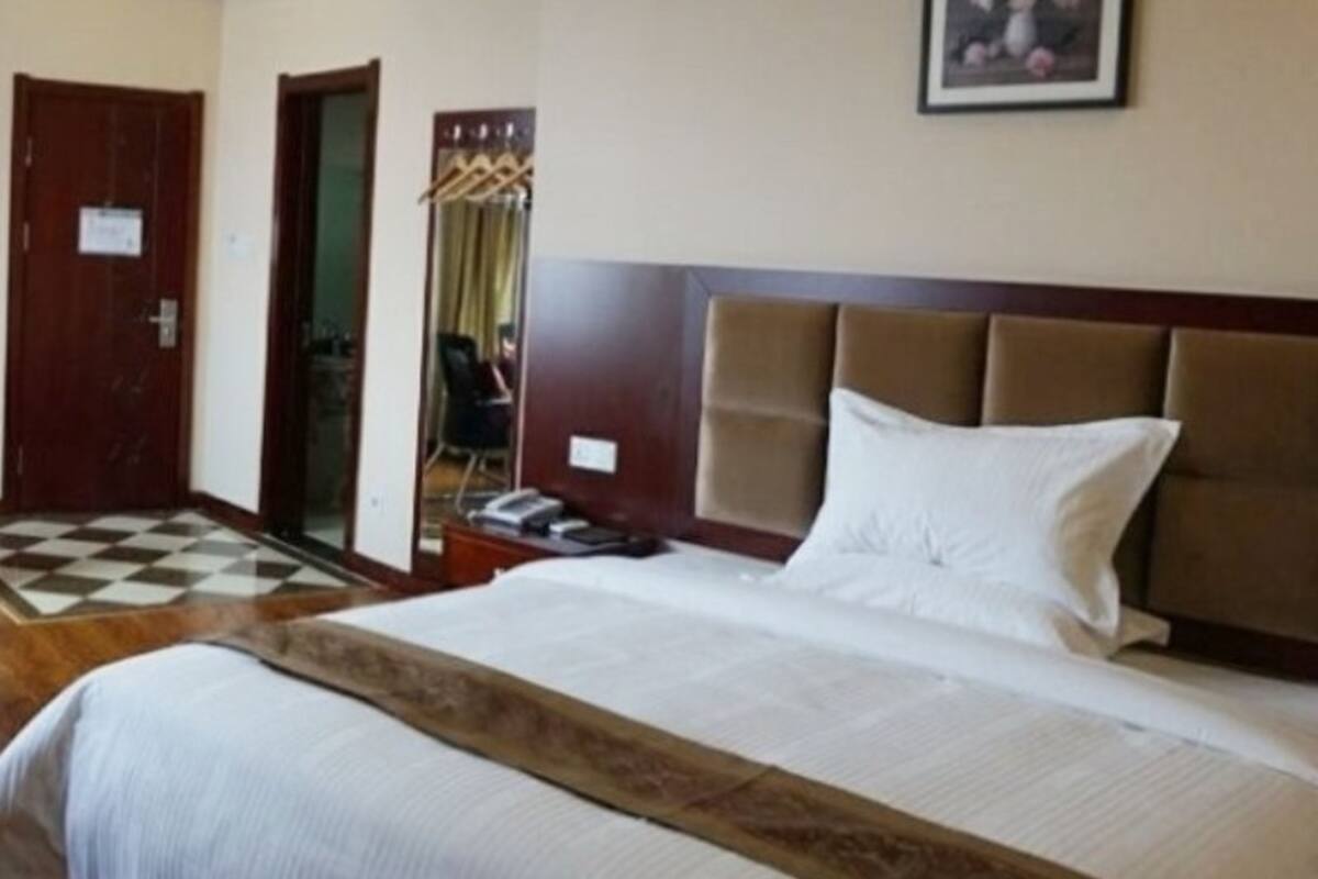Ein Hotelzimmer mit einem großen Bett, einem Holz-Kopfteil, einem Telefon und einem Spiegel an der Wand.