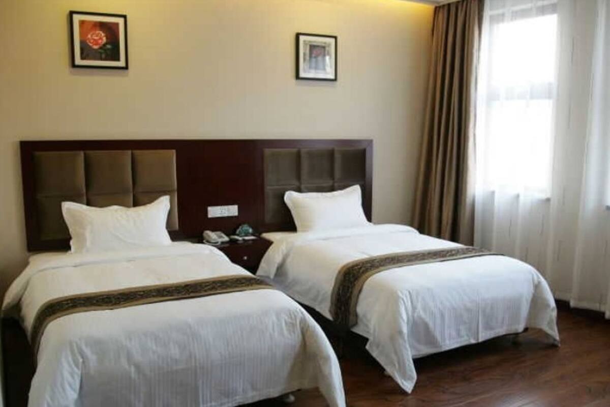 Ein Hotelzimmer mit zwei Betten, Holzboden und einem fenster mit Vorhängen.