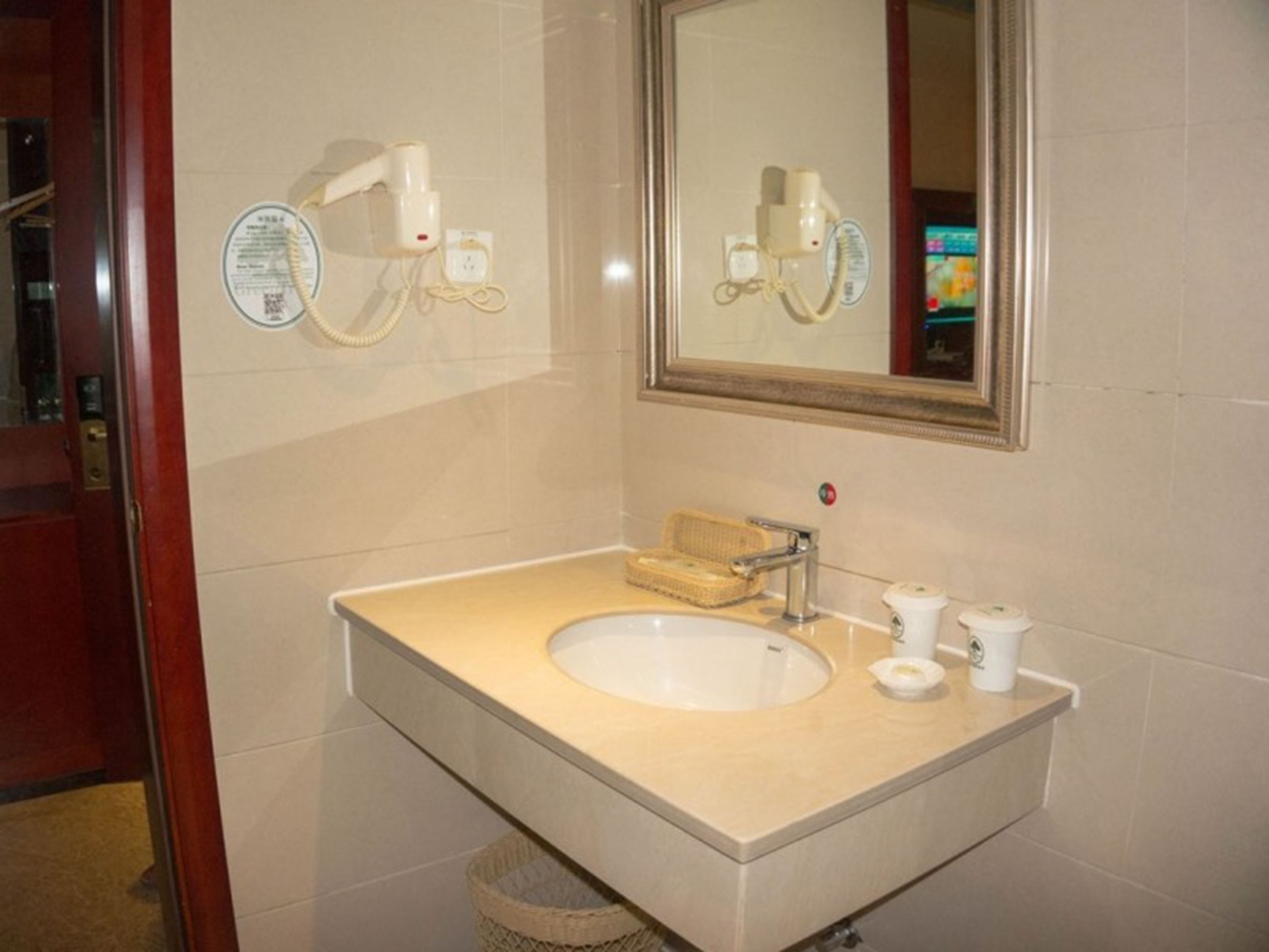 A bathroom with a beige sink, a mirror, and a hairdryer mounted on the wall.
