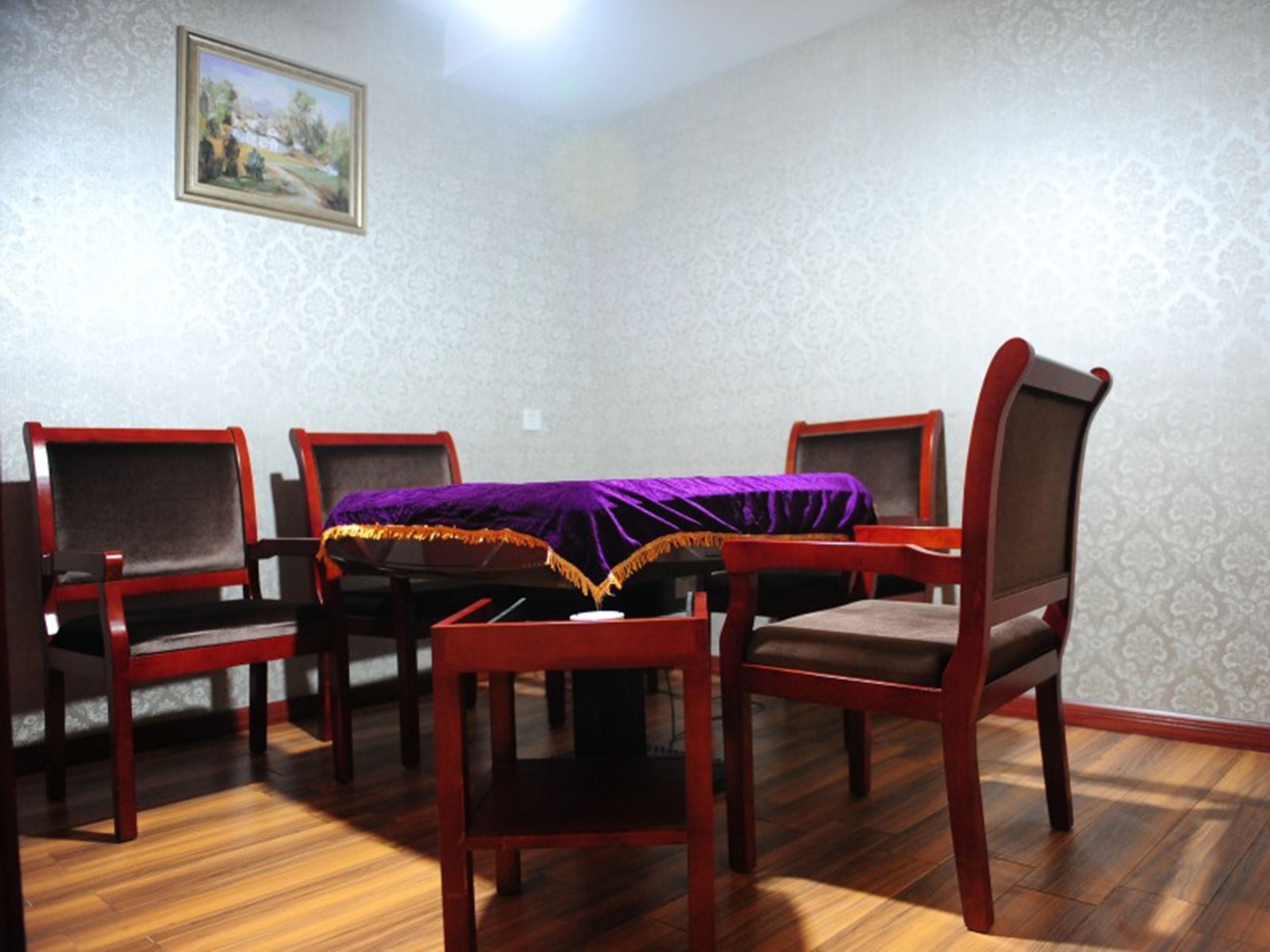 A dining room with a table covered by a purple cloth, surrounded by wooden chairs with cushioned seats.