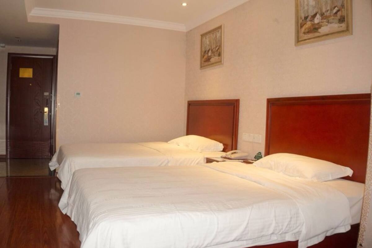 A hotel room with two beds, wooden headboards, and a painting on the wall.