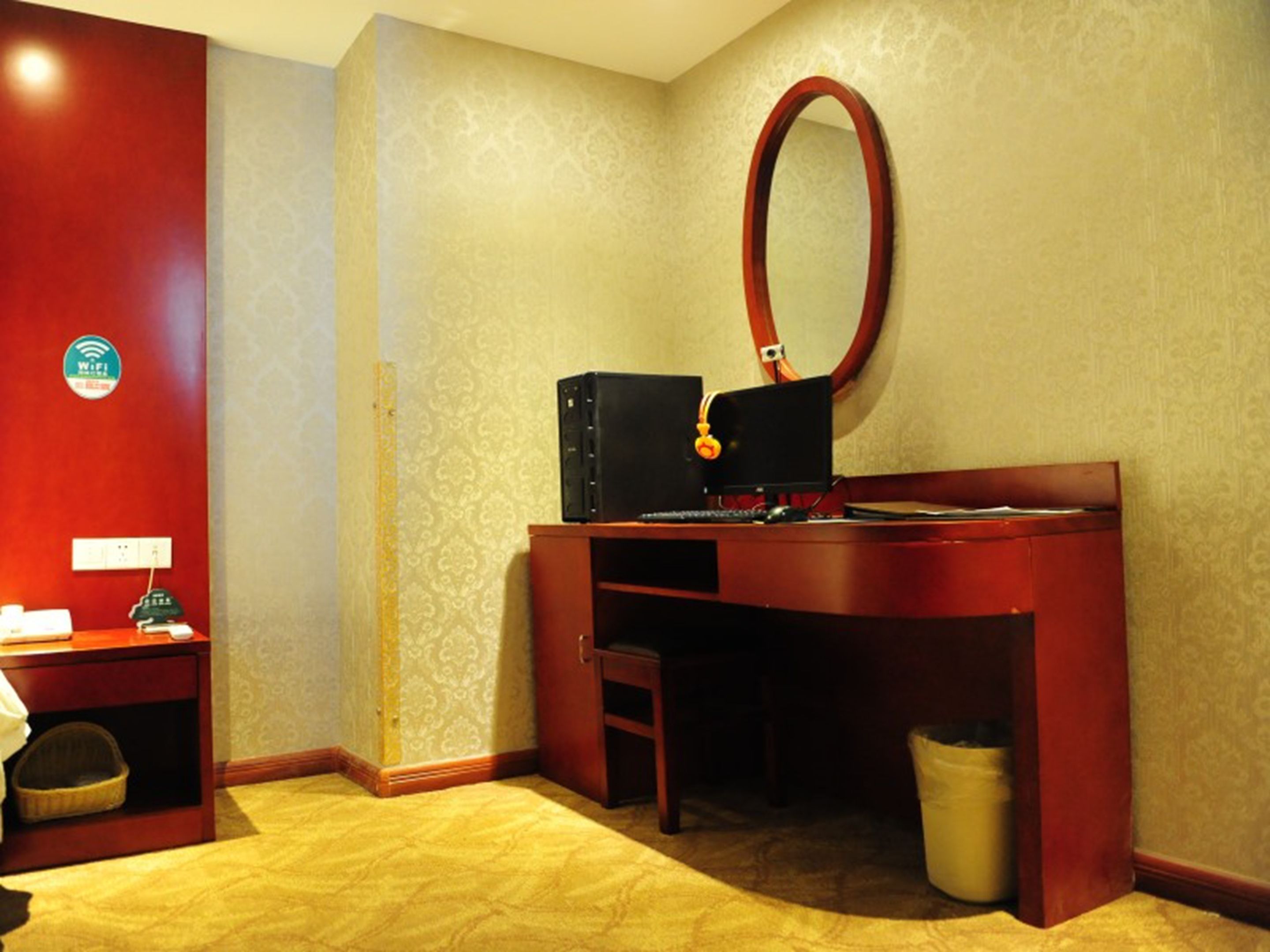 A hotel room with a desk, a computer, a mirror, a trash bin, and a small seating area.